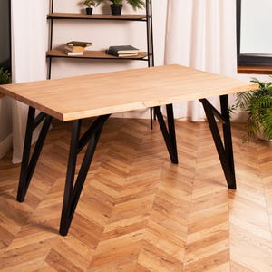 May include: A rectangular wooden table with a light brown surface and black metal legs. The table is approximately 60 inches long and 30 inches wide, with a modern design. The legs have a unique angled design, and the table is set on a wooden floor.