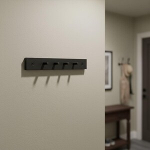 May include: A black, rectangular wall-mounted coat rack with five hooks. The hooks are evenly spaced along the bottom edge of the rack. The rack is mounted on a light beige wall.