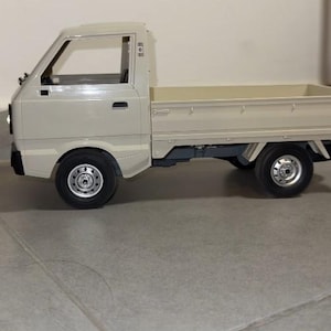 May include: A beige toy pickup truck with black tires and silver rims. The truck has a cab with a windshield and side windows, and a cargo bed. The truck is a miniature replica of a real vehicle.