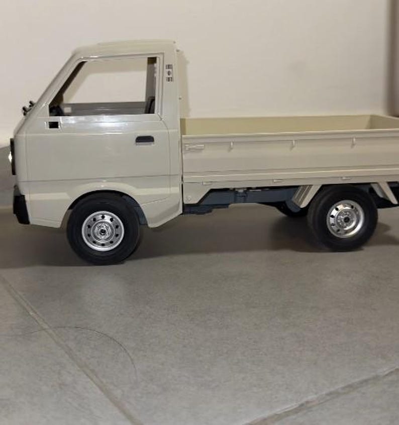 May include: A beige toy pickup truck with black tires and silver rims. The truck has a cab with a windshield and side windows, and a cargo bed. The truck is a miniature replica of a real vehicle.