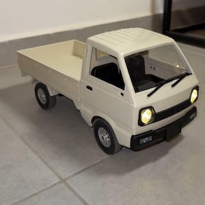 May include: A cream-colored toy pickup truck with a flatbed. The truck has black tires, a black front bumper, and clear windshield. The headlights are illuminated. The truck is sitting on a tiled surface.