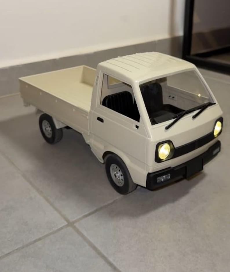 May include: A cream-colored toy pickup truck with a flatbed. The truck has black tires, a black front bumper, and clear windshield. The headlights are illuminated. The truck is sitting on a tiled surface.