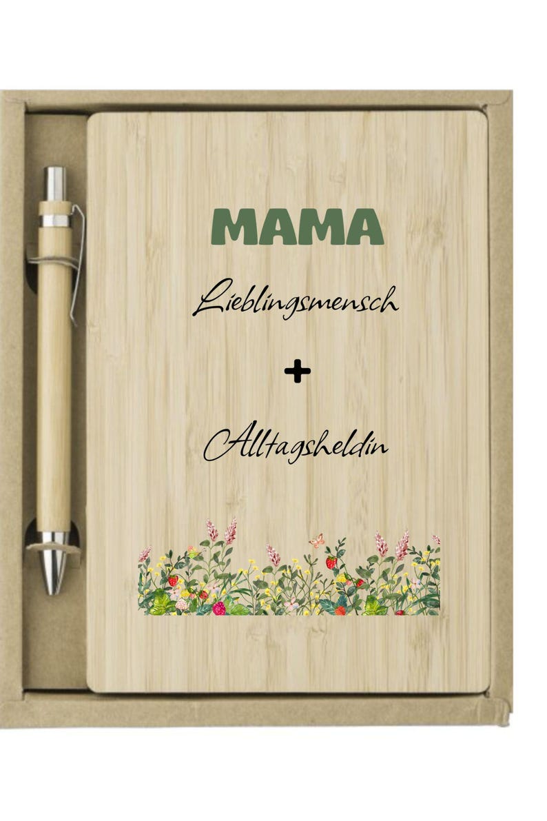 May include: A wooden notepad and pen set. The notepad has the word "MAMA" in green, with "Lieblingsmensch + Alltagsheldin" written below. A floral design is at the bottom. The pen is light brown.