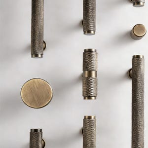 May include: An assortment of bronze-colored cabinet hardware, including cylindrical knobs and pulls. The hardware features a textured, diamond-patterned surface. Various sizes and shapes are displayed against a white background, showcasing the design options.