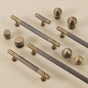 Puede incluir: Un surtido de herrajes de gabinete de latón antiguo, que incluyen tiradores de barra, perillas y tiradores cilíndricos. Los tiradores tienen una sección central acanalada y son de varios tamaños. Las perillas son esféricas con un diseño acanalado.
