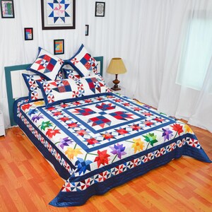 Könnte beinhalten: Eine weiße und blaue Patchwork-Decke mit einem Blumendesign in Rot-, Orange-, Gelb-, Grün-, Blau- und Violetttönen. Die Decke liegt auf einem Bett mit passenden Kissenbezügen und Kissen.