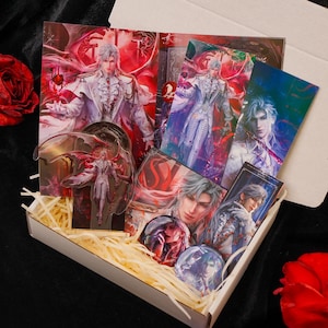May include: A gift box filled with fantasy-themed merchandise. Includes art prints, acrylic standees, and pinback buttons featuring a character with silver hair and a white outfit. The artwork has a red and white color scheme.