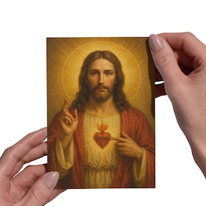 May include: A religious portrait depicting a man with long brown hair and a beard, wearing a red robe and a white tunic. A golden halo surrounds his head. A flaming heart is on his chest. The man is pointing to the heart.