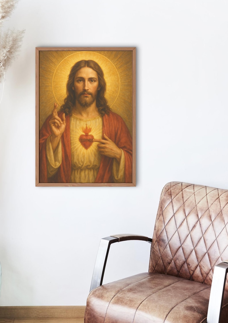 May include: A framed religious portrait depicts a man with long brown hair, a beard, and a halo. He wears a red robe and points to a flaming heart on his chest. The artwork is displayed on a white wall near a brown leather chair.