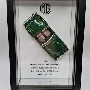 May include: A framed display featuring a dark green MGA model car viewed from above. The display includes the MG logo and technical specifications: MGA, ENGINE: 1.5L NATURALLY ASPIRATED, POWER: 72 bhp, TORQUE: 77 lb-ft, 0-60: 15.7 sec, TOP SPEED: 98 mph, YEAR: 1955-1959.