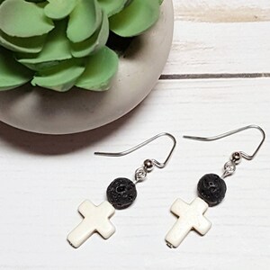 May include: A pair of silver earrings with a white cross charm and a black lava bead on each earring.