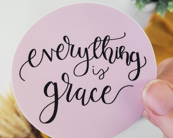Puede incluir: Una pegatina redonda rosa con el texto "everything is grace" escrito en cursiva negra.