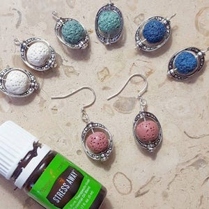 May include: An assortment of silver-toned pendants and earrings featuring porous, spherical beads in various colors, including white, teal, blue, and pink. A bottle of essential oil with the text "STRESS AWAY" is also present.