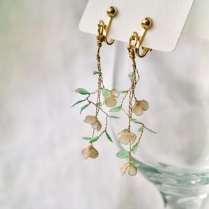 May include: A pair of gold clip-on earrings with delicate green leaves and white flowers dangling from them.