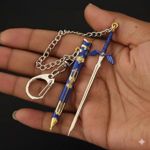 May include: A miniature sword and sheath keychain. The sword has a silver blade and blue hilt with gold accents. The sheath is blue with gold detailing. A silver chain and keyring are attached.