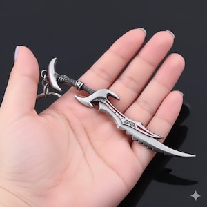 May include: A silver-colored sword-shaped keychain with a decorative handle and a red accent on the blade. The keychain has a crescent moon-shaped top and a detailed design.
