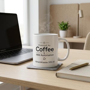 Op de afbeelding: Een witte keramische mok met een handvat, voorzien van zwarte tekst met de tekst Powered by Coffee & Mild Automation, een aan-uit icoon, een klein koffiekopje icoon en de tekst Keramiktasse 325 ml gedrukt op de voorzijde van de mok.