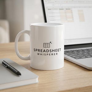 Könnte beinhalten: Ein weißer Keramikbecher mit einer schwarzen Grafik eines Tabellenrasters und zwei kleinen Sternen darüber. Der Text SPREADSHEET WHISPERER ist in schwarzen Großbuchstaben unter dem Raster aufgedruckt. Der Becher hat einen geschwungenen Henkel.
