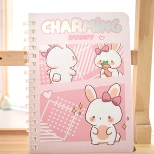 May include: A pink spiral bound notebook with a white bunny holding a carrot on the cover. The cover also has the text "Charming Bunny" in silver glitter.