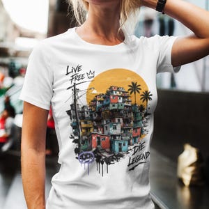 May include: White t-shirt featuring a colorful graphic of a cityscape with the text "LIVE FREE" and "DIE LEGEND". The design includes a yellow sun, palm trees, and graffiti-style accents.