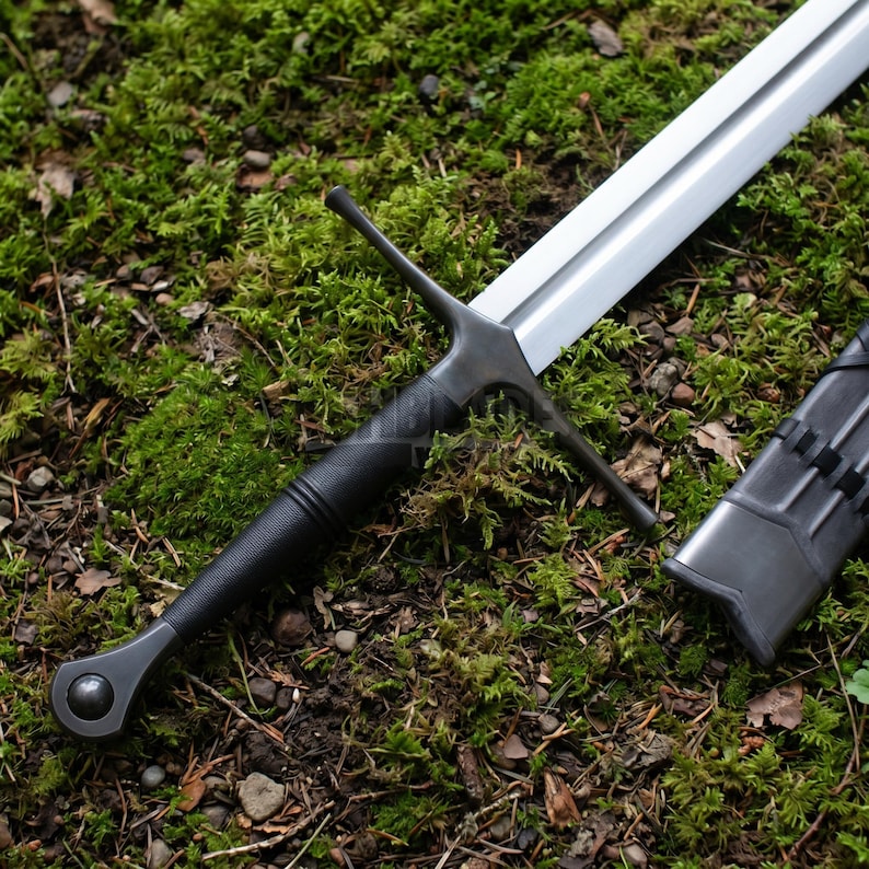 May include: A longsword with a polished silver-colored steel blade and a black textured grip. The sword features a straight crossguard and a rounded pommel with a central circular detail. A matching black scabbard lies beside the sword.
