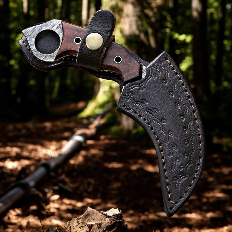 Pu&ograve; includere: Un coltello curvo con manico in legno scuro e lama argentata. Il coltello &egrave; in un fodero di pelle nera con cuciture decorative. Un cinturino in pelle nera con un bottone in ottone fissa il coltello. Lo sfondo &egrave; una scena di foresta sfocata.