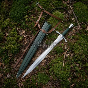 May include: A steel sword with a dark green grip and crossguard, accompanied by a matching dark green scabbard and a brown leather harness with silver-toned metal buckles and rings, designed for carrying the weapon securely.