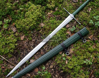 Puede incluir: Una espada larga de acero con hoja de doble filo, guarda plateada y empuñadura verde con un pomo circular. Junto a la espada se encuentra una vaina verde a juego con estrías verticales y correas de cuero negro con anillos metálicos.