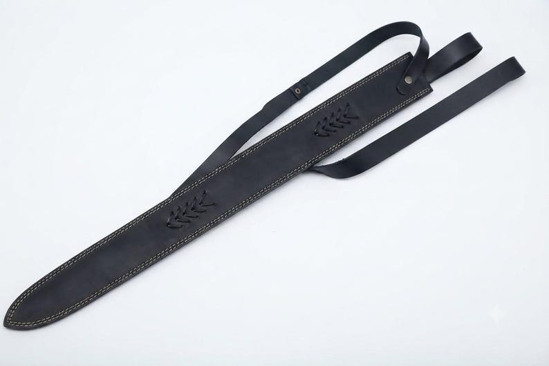 May include: A black leather sword scabbard featuring light-colored contrast stitching along the edges, decorative braided leather accents, and an integrated adjustable strap system with a metal rivet for secure attachment and carrying.