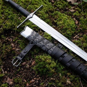 May include: A long steel sword with a straight double-edged blade and a black grip, paired with a black leather scabbard. The scabbard features a silver-colored metal throat, decorative leather lacing, and an integrated belt strap with a buckle.