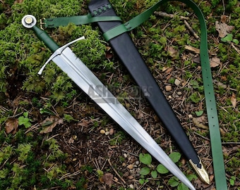 May include: A steel sword with a green hilt and a crossguard, accompanied by a black scabbard featuring a gold-toned metal tip. A long green leather strap is attached to the scabbard, which includes a metal buckle for adjustment and secure fastening.