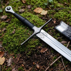 May include: A steel sword with a black wrapped grip, a circular pommel, and a straight crossguard. The blade features a central fuller and a metallic finish. A matching black and silver scabbard tip is positioned next to the sword blade.
