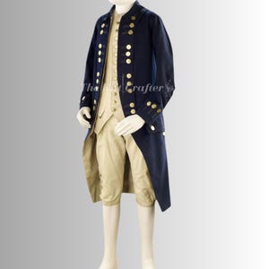 以下が含まれることがあります： 金色のボタンが付いた、ネイビーブルーのコロニアルスタイルのコスチューム。ロングコート、ベスト、膝丈の半ズボンが含まれています。コートは燕尾服のデザインです。マネキンに着せられています。