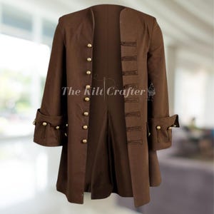 May include: A brown coat with gold buttons and decorative cuffs. The coat has a high collar and a long, tailored design. The text "The Kilt Crafter" is visible on the coat.