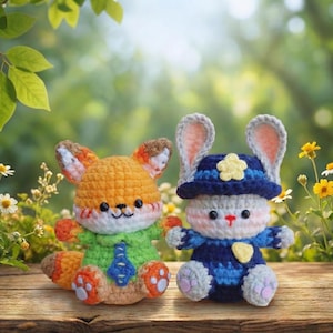 May include: Two crocheted stuffed animals: an orange fox wearing a green shirt and a blue tie, and a gray bunny wearing a blue police hat and uniform. The toys are sitting on a wooden surface with a blurred green background.