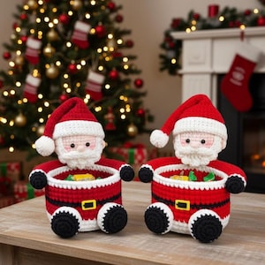 May include: Two handmade crochet Santa Claus baskets. Each basket is red with white trim, a black belt with a gold buckle, and black feet. The Santa faces have white beards and red hats. The baskets are filled with colorful candies. Christmas decor.
