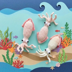 May include: Three crocheted squid toys in light pink and cream colors. Each squid features a textured, rounded body, multiple dangling tentacles, and two prominent black and white plastic eyes. The toys are arranged in a cluster.