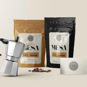 Puede incluir: Una cafetera italiana de aluminio con un asa negra se encuentra junto a dos bolsas de café y una tarjeta de visita. Las bolsas están etiquetadas como "Golden Mesa" con café "Hula Washed". Granos de café esparcidos delante.