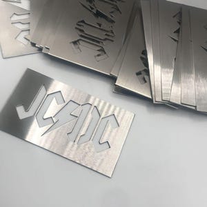 May include: A stack of metal stencils with the word "J.C.A.I.C." cut out. The stencils are silver and have a brushed finish.