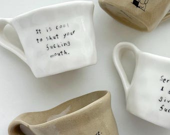May include: Four ceramic mugs in white and tan. One white mug has the text "It is cool to shut your fucking mouth." Another has "Ser I don't give a fuck." A tan mug reads "Don't be a slave. Be a happy slave."