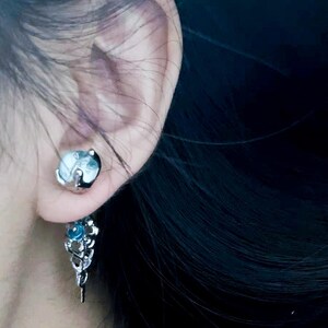 May include: A silver dangle earring with a blue gemstone and a leaf design.
