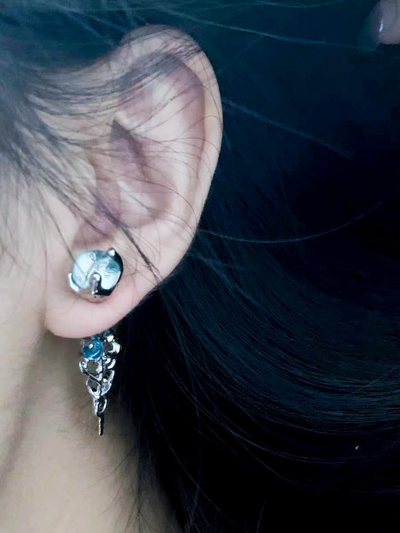 May include: A silver dangle earring with a blue gemstone and a leaf design.