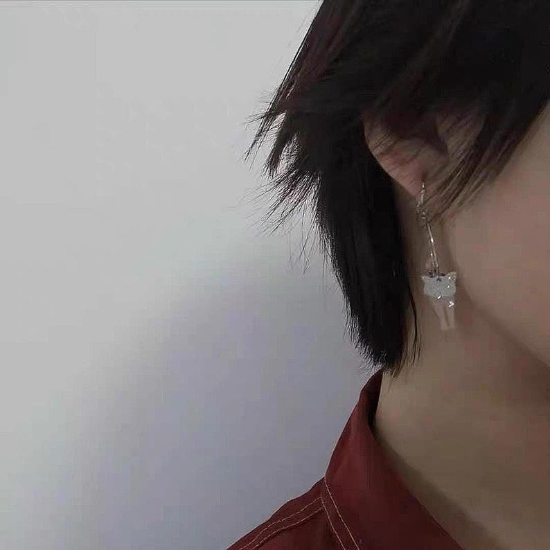 May include: A person with short black hair wearing a red shirt with a white butterfly earring.
