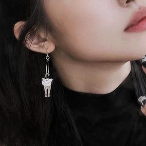 May include: Silver cat dangle earrings with a hoop design. The cat is facing forward with a white face and black eyes.