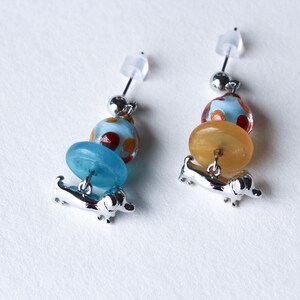 May include: A pair of silver dangle earrings with a blue and orange glass bead design and a silver dachshund charm.