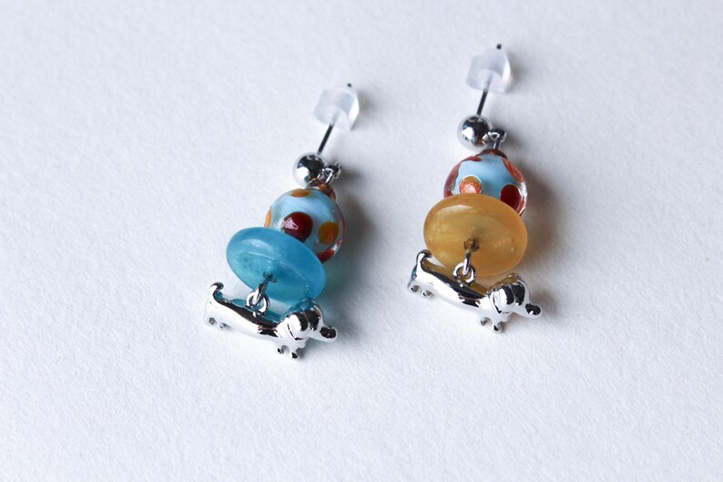May include: A pair of silver dangle earrings with a blue and orange glass bead design and a silver dachshund charm.