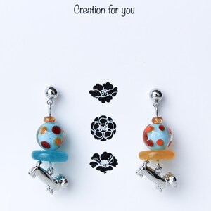 May include: A pair of earrings featuring a blue and orange glass bead with white polka dots, a silver dachshund charm, and a silver post.