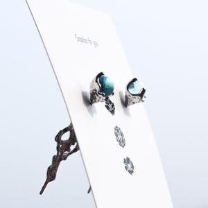 May include: A pair of silver earrings with blue glass stones. The earrings are displayed on a white card with the text "Creation for you".