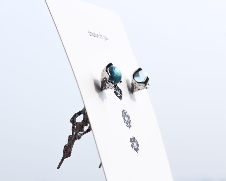 May include: A pair of silver earrings with blue glass stones. The earrings are displayed on a white card with the text "Creation for you".