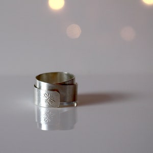 May include: A silver ring with a bee design. The ring is made of multiple bands of metal that are twisted together.